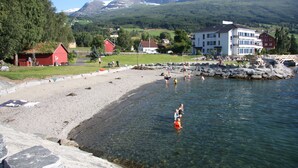 Et kystområde med klart vand, en klippefyldt kystlinje og bygninger i baggrunden.