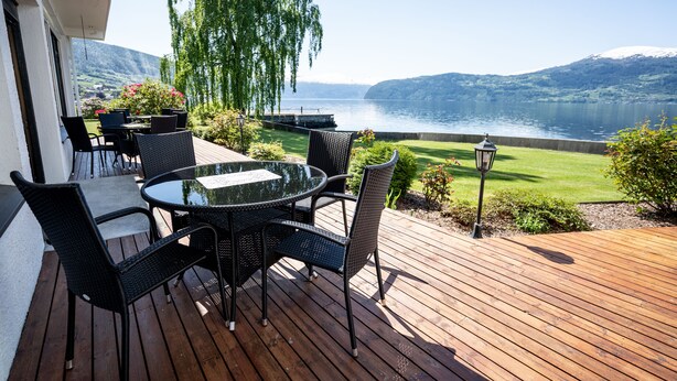 En træterrasse med et bord og stole, udsigt over en sø og bjerge.