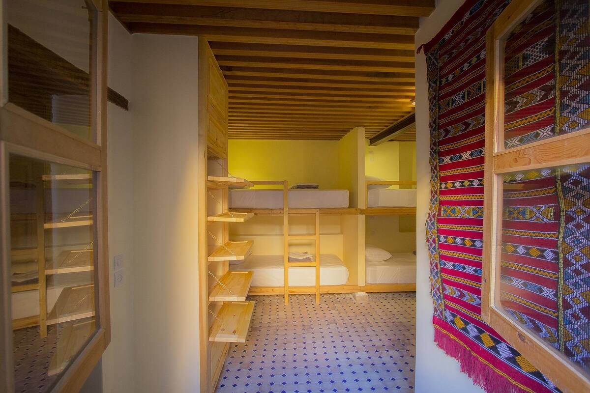 Una habitación con literas, un ventanal con cortinas estampadas y suelo de baldosas.