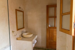 A bathroom with a wooden door, a mirror, a sink with a bowl, and a towel rack.