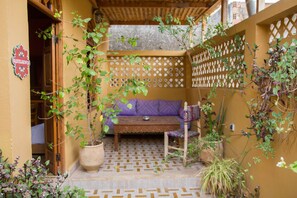 A cozy outdoor seating area with a wooden bench and cushions, surrounded by plants and a lattice wall. - Medina Social Club - Riad (Fes)