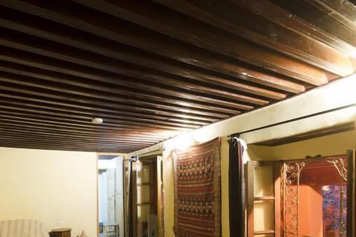 Una habitación con dos camas, vigas de madera en el techo y una cortina estampada.