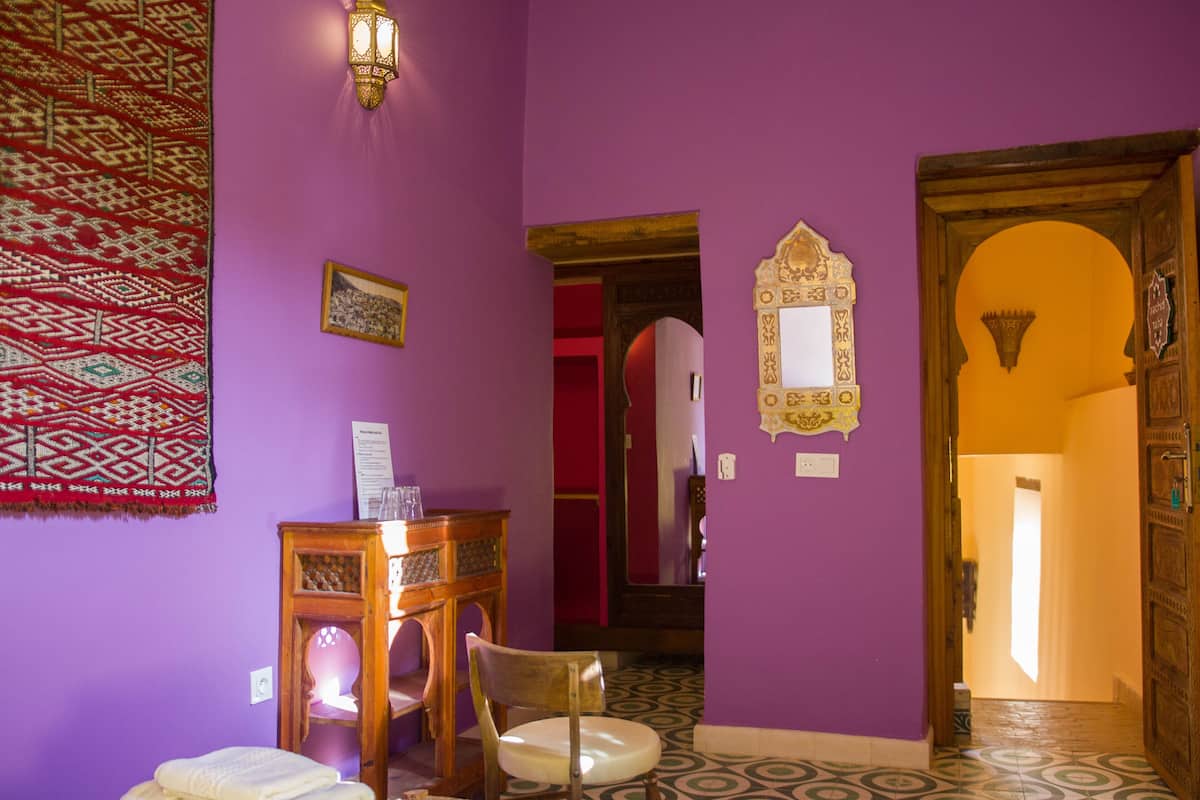 Una habitación con paredes moradas, una silla de madera, una mesita y una alfombra estampada.