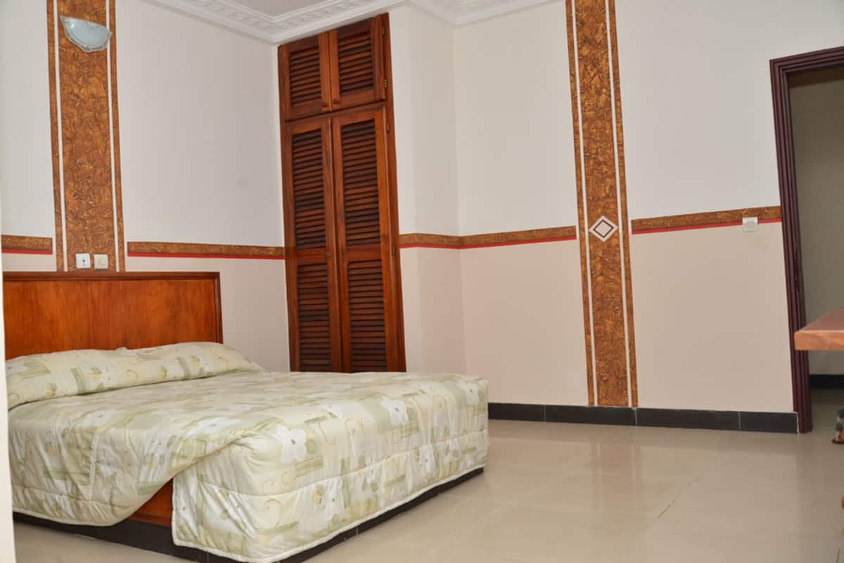 A bedroom with a bed, wooden wardrobe, and decorative wall paneling.
