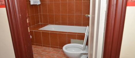 Une salle de bain avec une baignoire, des toilettes et un carrelage au sol.