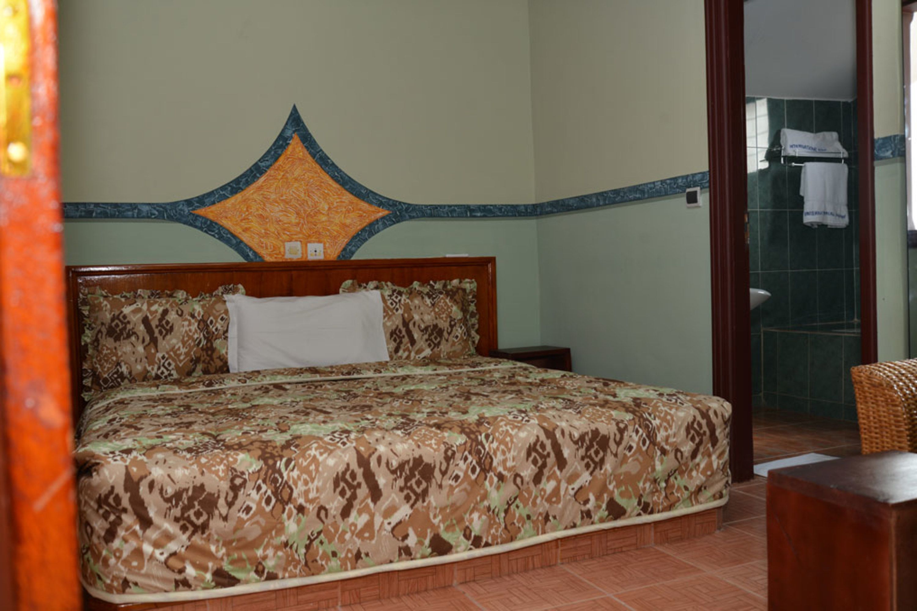 A neatly made bed with a patterned bedspread, a wooden headboard, and a wall with a decorative molding.