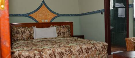 A neatly made bed with a patterned bedspread, a wooden headboard, and a wall with a decorative molding.