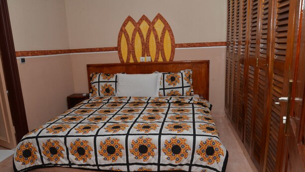Une chambre à coucher comprenant un lit, une tête de lit, une table de chevet et une porte en bois dotée de panneaux à persiennes.
