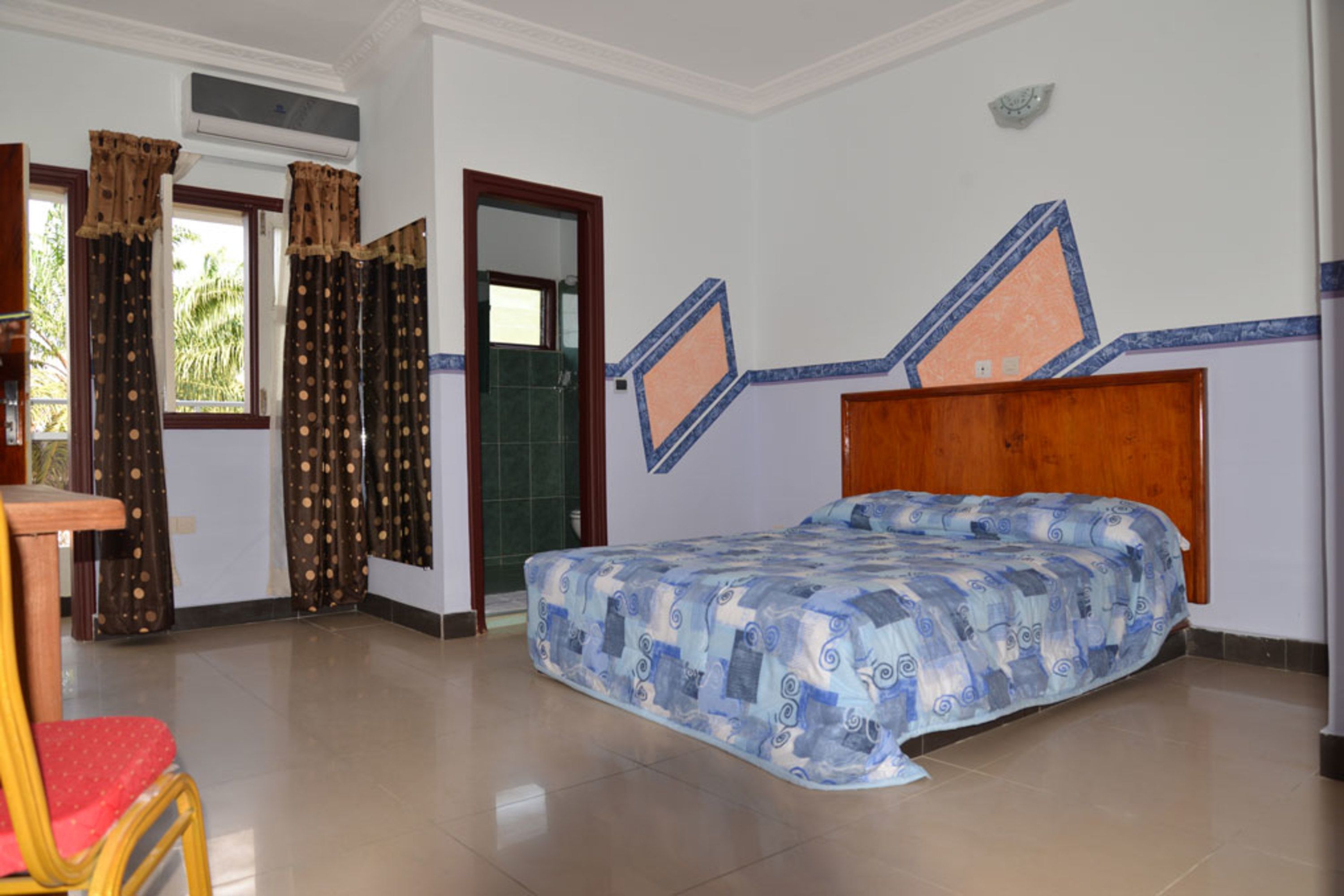 Een slaapkamer met een bed, gordijnen, een houten stoel en een betegelde vloer.