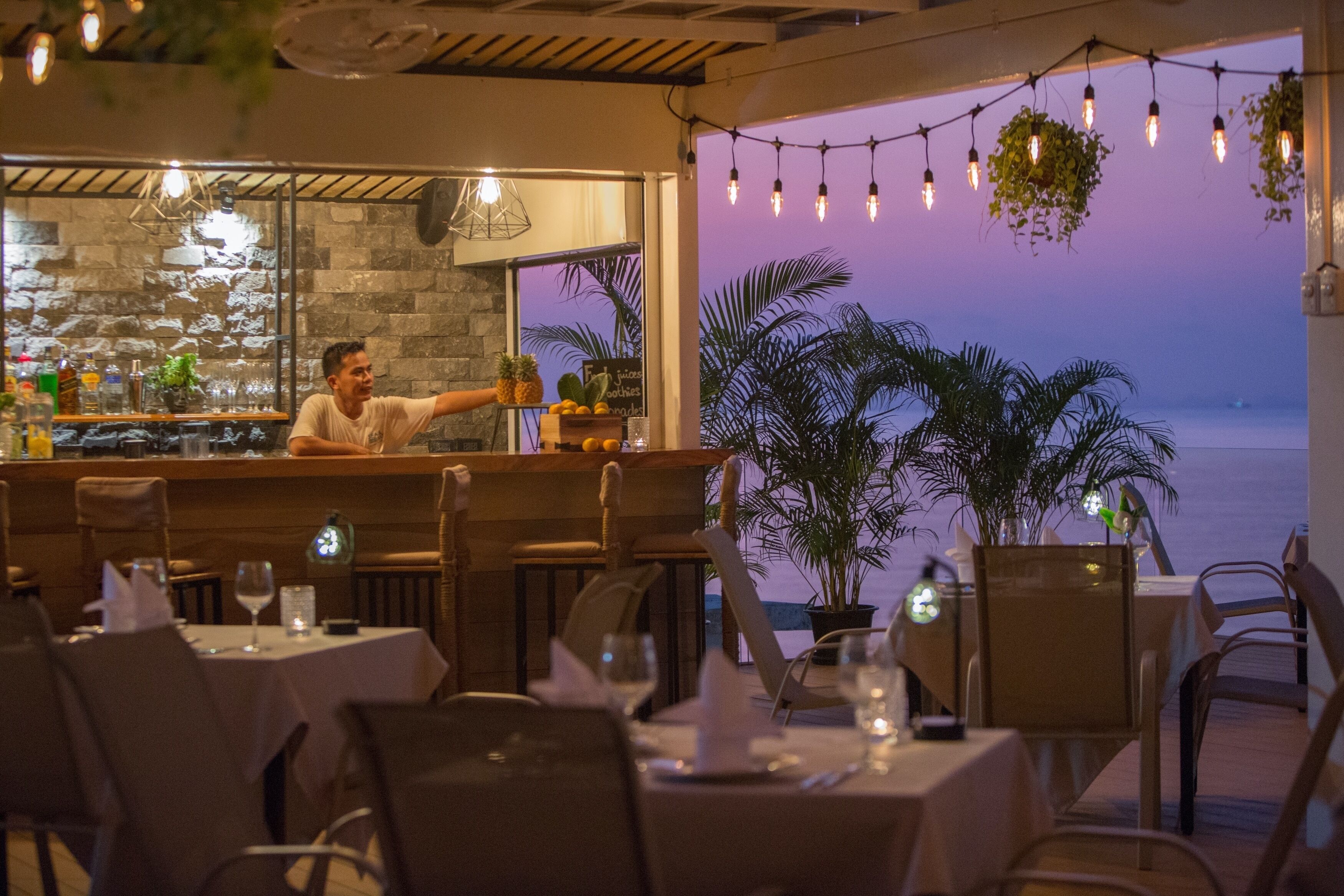 Un ristorante con zona bar, tavoli, sedie e vista sull'oceano.