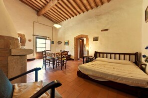 Una habitación con una cama, una mesa de comedor con sillas, una chimenea de piedra y piso de baldosas.