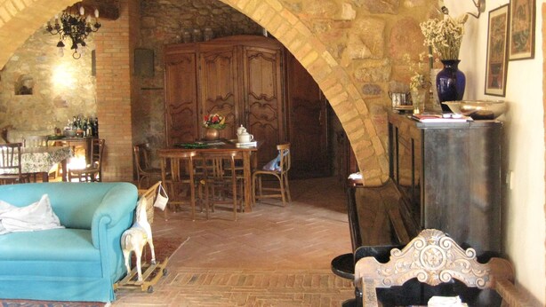 A stone-walled room with a wooden table, chairs, a sofa, and a decorative horse figure. - Agriturismo Il Casalino (Civitella Paganico)