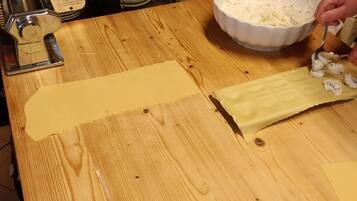 A kitchen counter with a pasta machine, a bowl of dough, and a person preparing dough.