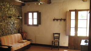 A rustic room with a stone wall, a wooden ceiling, a striped sofa, a wooden chair, and a window with shutters. - Agriturismo Il Casalino (Civitella Paganico)