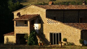 A stone building with a tiled roof, a staircase leading to a balcony, and potted plants around the entrance. - Agriturismo Il Casalino (Civitella Paganico)
