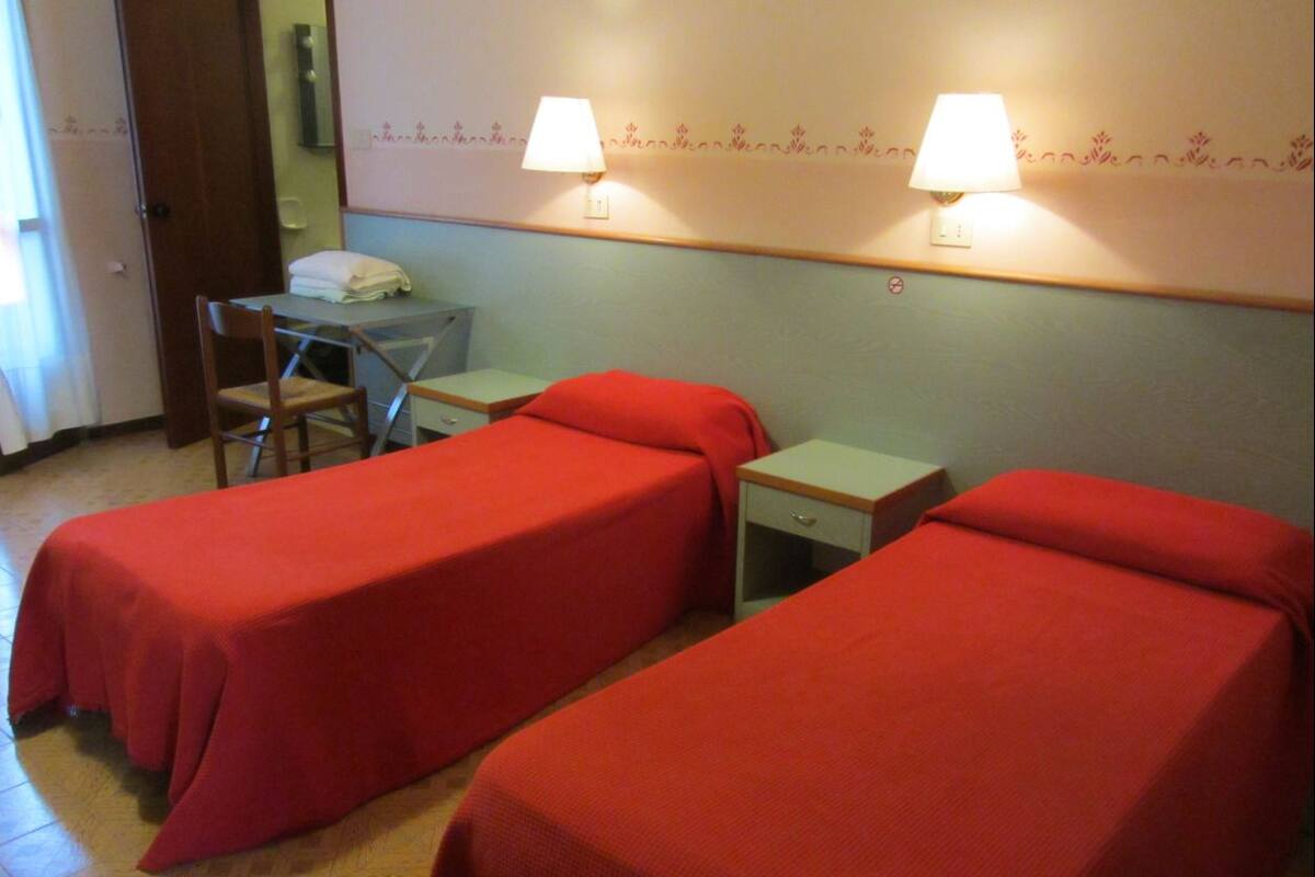 A room with two single beds, a small table, a chair, and two bedside lamps.