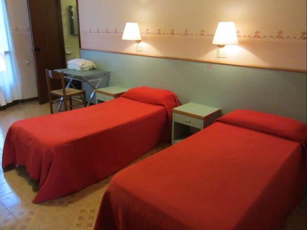 A room with two single beds, a small table, a chair, and two bedside lamps.