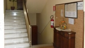 A staircase leading to a landing with a fire extinguisher and a bulletin board. - Locanda Gaia (Muggia)
