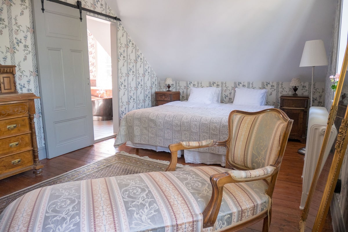 A bedroom with a bed, a chair, a dresser, and a lamp.