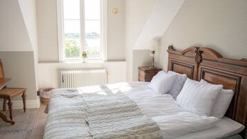 A bedroom with a large bed, a wooden headboard, a window with a view, a radiator, and a bedside table with a lamp.