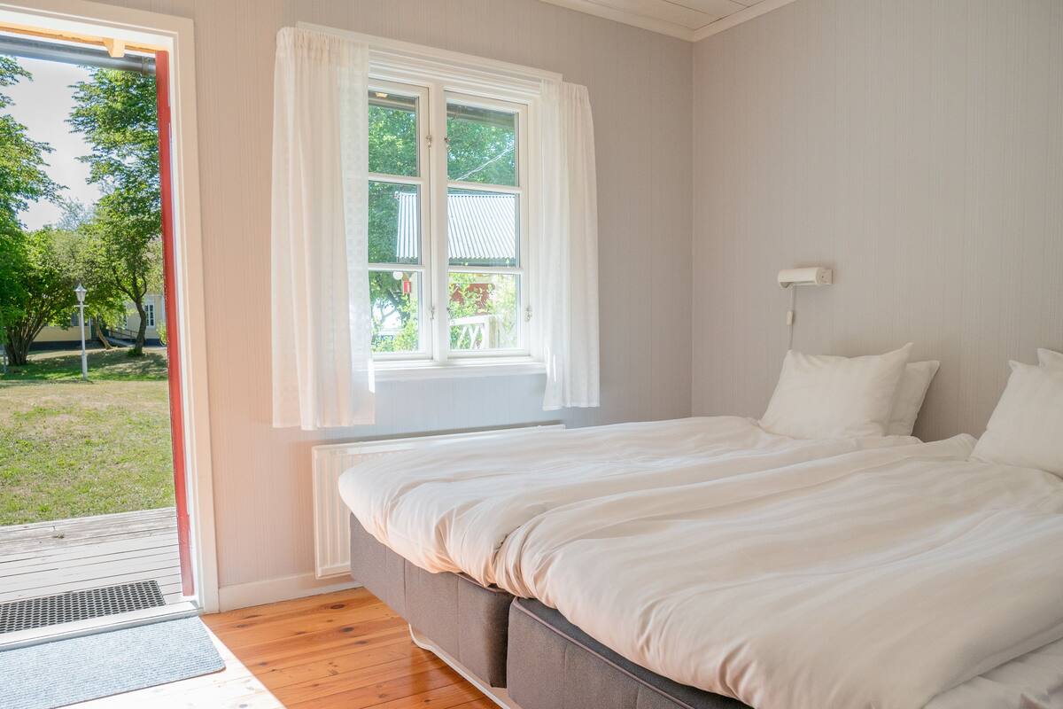 A bedroom with a bed, a window with curtains, a radiator, and a view of the outdoors.