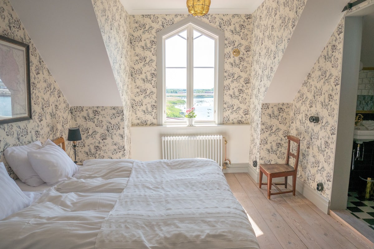 A bedroom with a large bed, a window with a view, a radiator, and a chair.