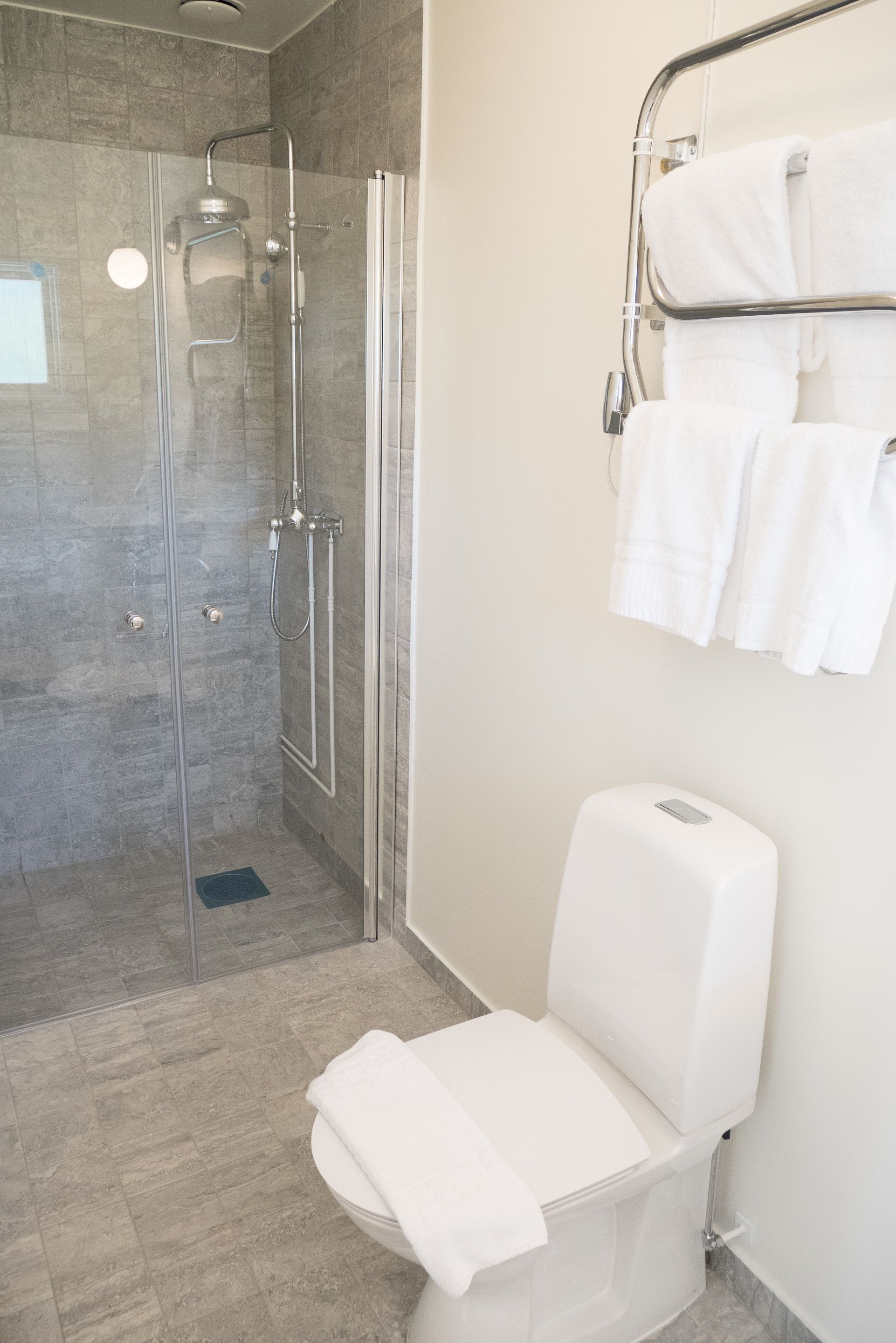 A modern bathroom with a glass-enclosed shower, a white toilet, and a towel rack with multiple towels.