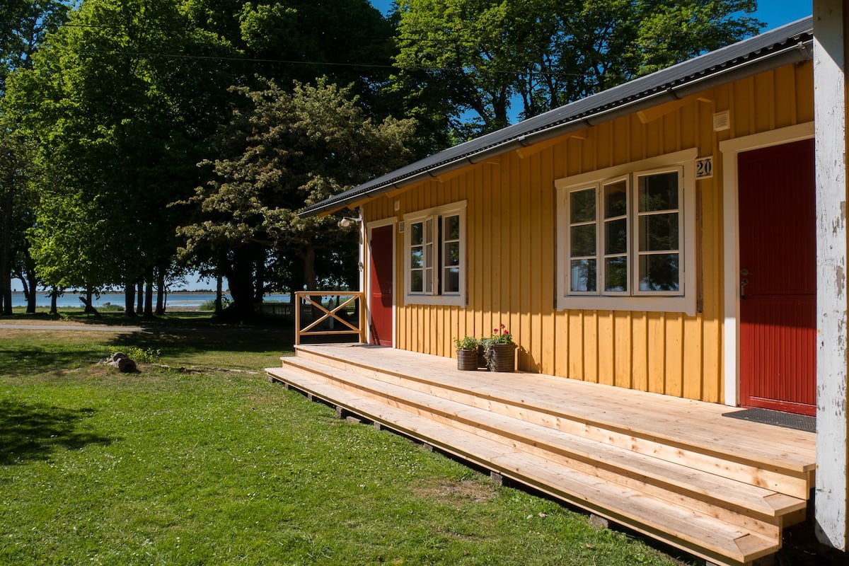A wooden cabin with a red door, a set of stairs leading to a porch, and a view of a lake.