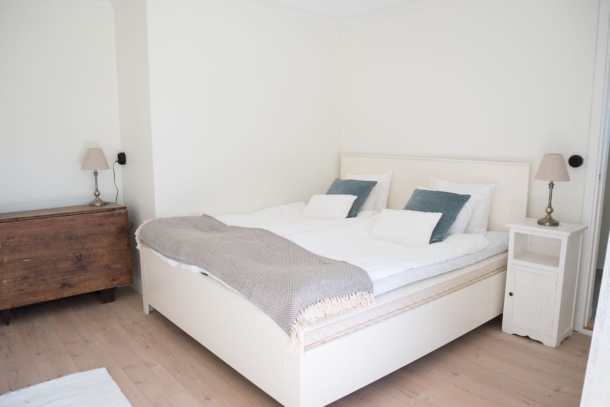 A neatly arranged bedroom with a bed, bedside tables, and a wooden dresser.