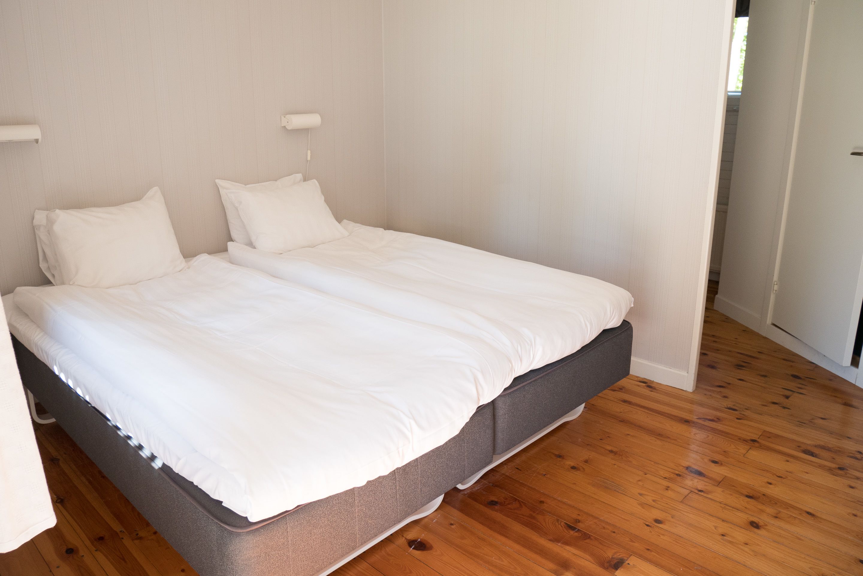 Ein Doppelbett mit weißer Bettwäsche in einem Zimmer mit Holzboden und weißen Wänden.