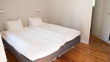 Ein Doppelbett mit weißer Bettwäsche in einem Zimmer mit Holzboden und weißen Wänden.