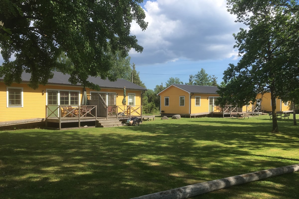 A row of yellow cabins with wooden decks and outdoor seating, surrounded by well-maintained grass and trees.