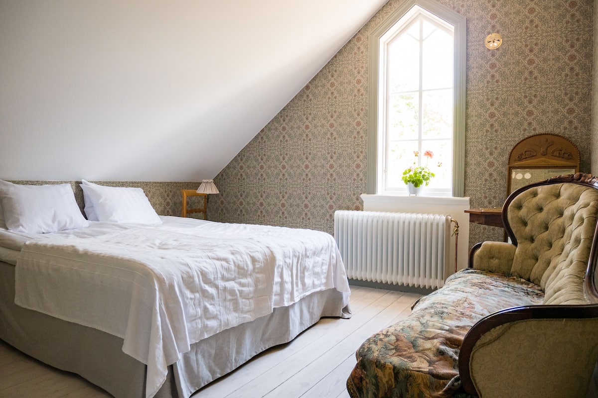 A bedroom with a bed, a chair, a radiator, and a window with a plant.