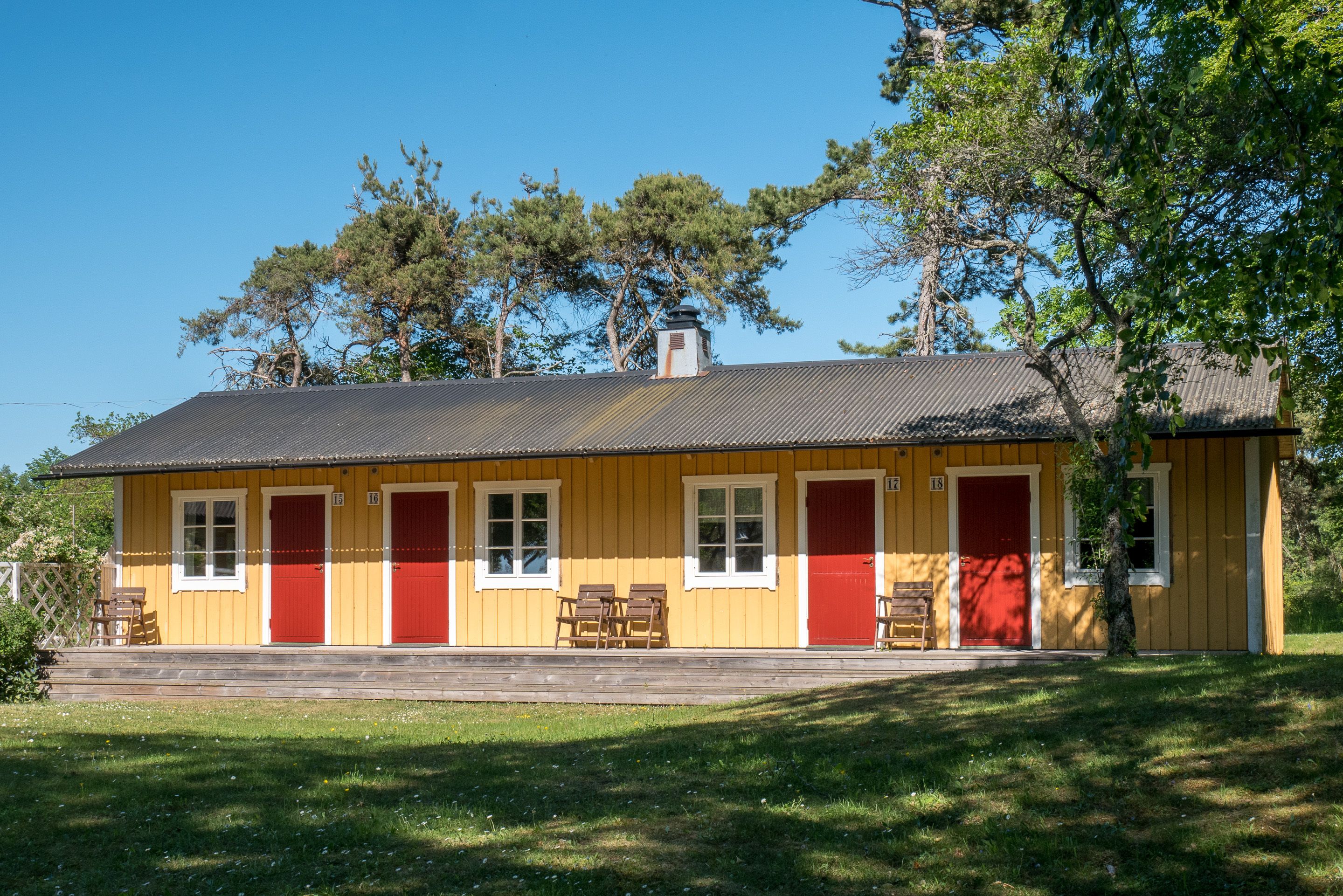 A yellow building with red doors and windows, a chimney, and a wooden bench outside.
