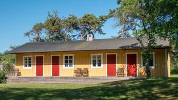Un bâtiment jaune avec des portes et des fenêtres rouges, une cheminée et un banc en bois à l’extérieur.