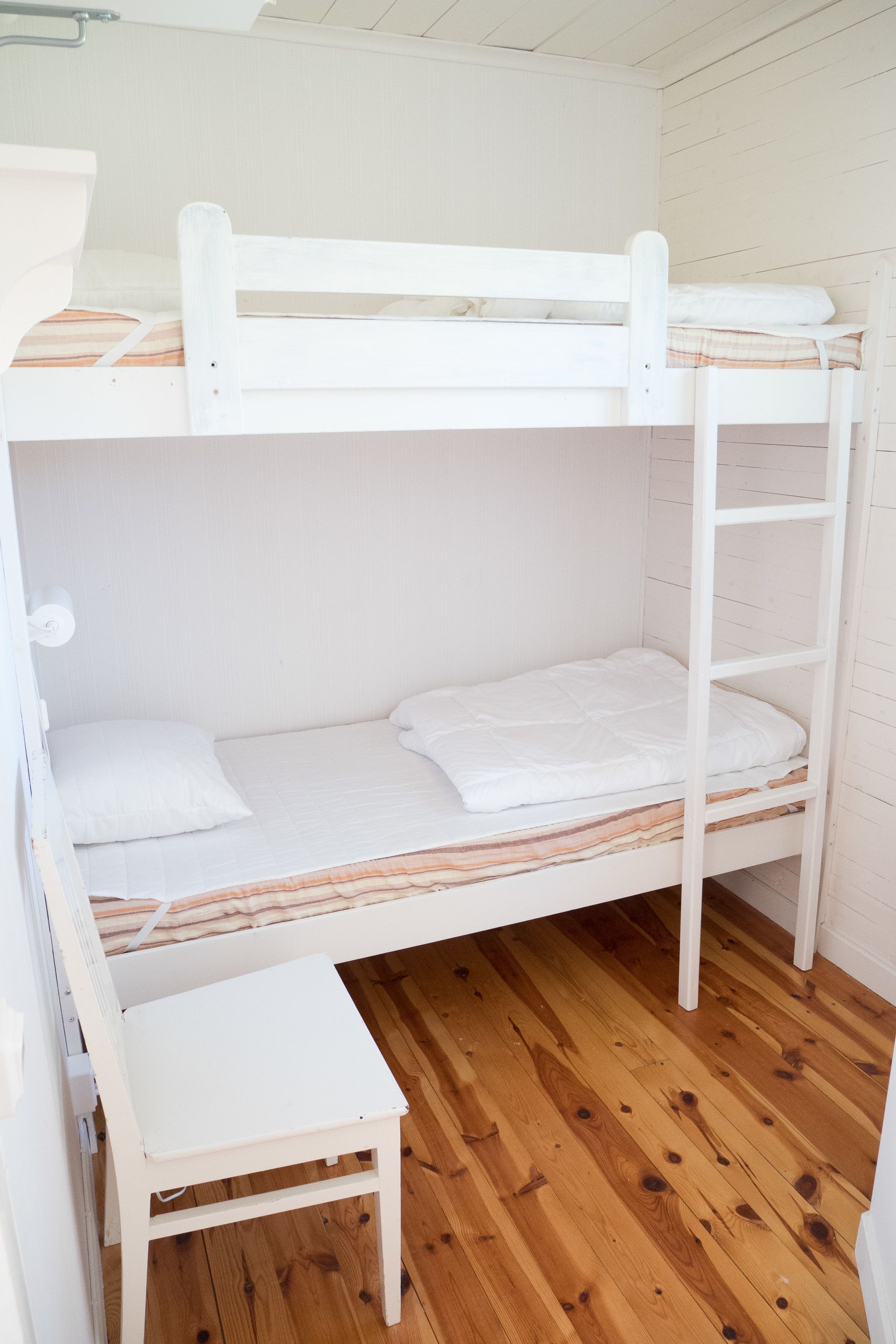 Una cama litera con estructura blanca y suelo de madera.
