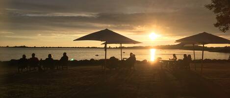 Sonnenuntergang mit Personen, die unter Sonnenschirmen am See sitzen.