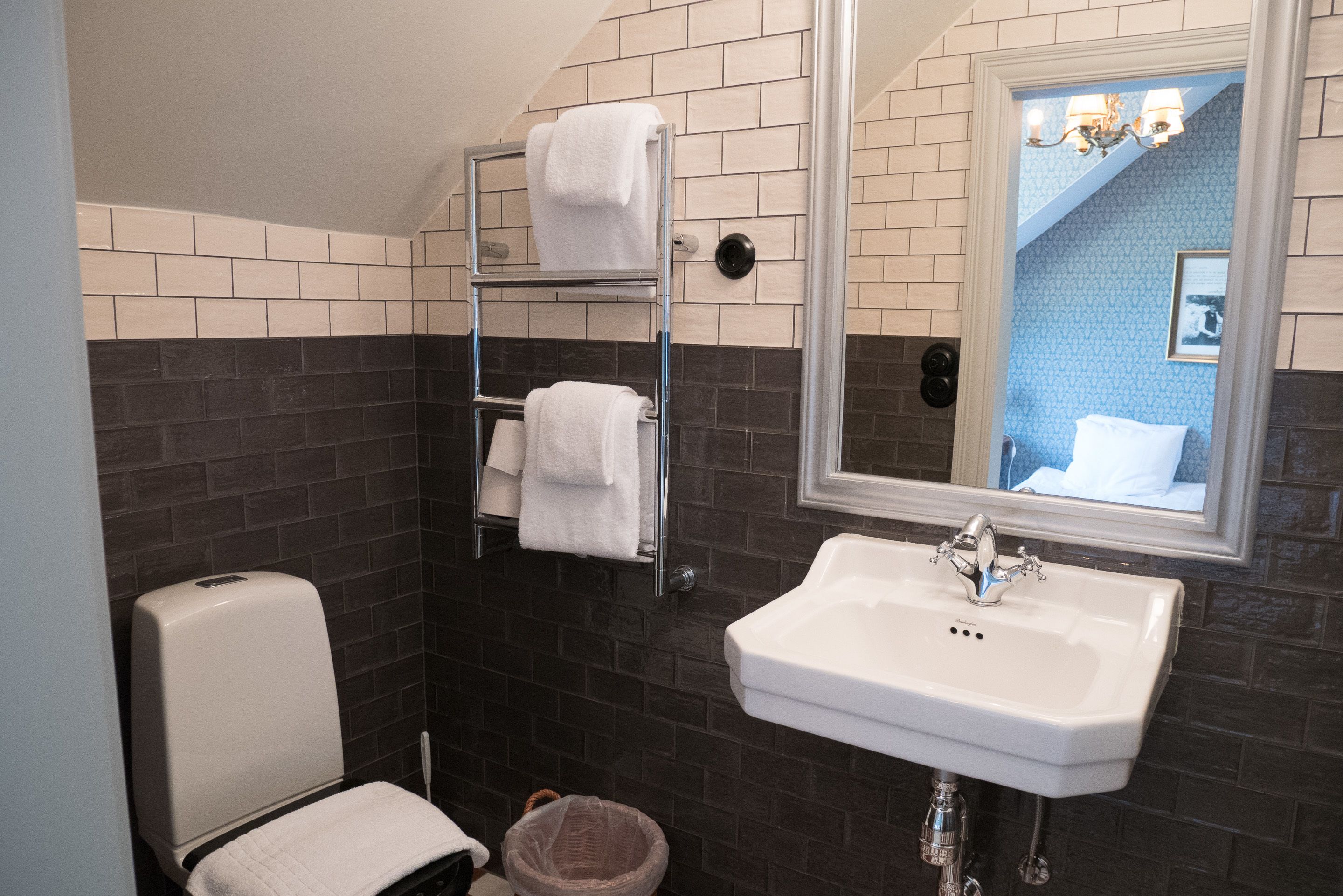 A bathroom with a white sink, a towel rack, a hand dryer, and a trash bin.