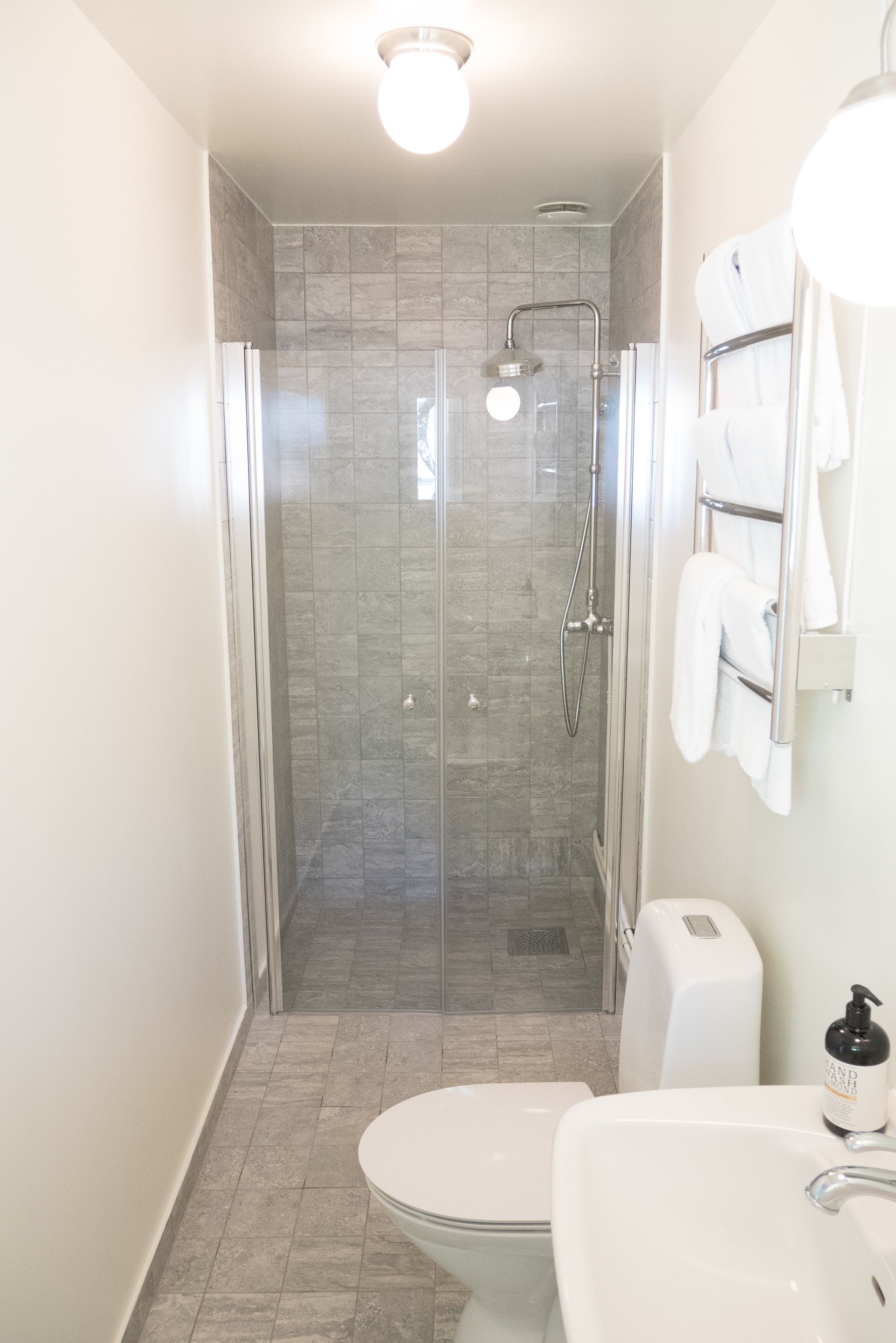 Un baño moderno con ducha envuelta en vidrio, inodoro y lavamanos con dispensador de jabón.