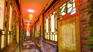 Un couloir étroit, avec des portes et des fenêtres en bois, un banc et des lanternes suspendues.
