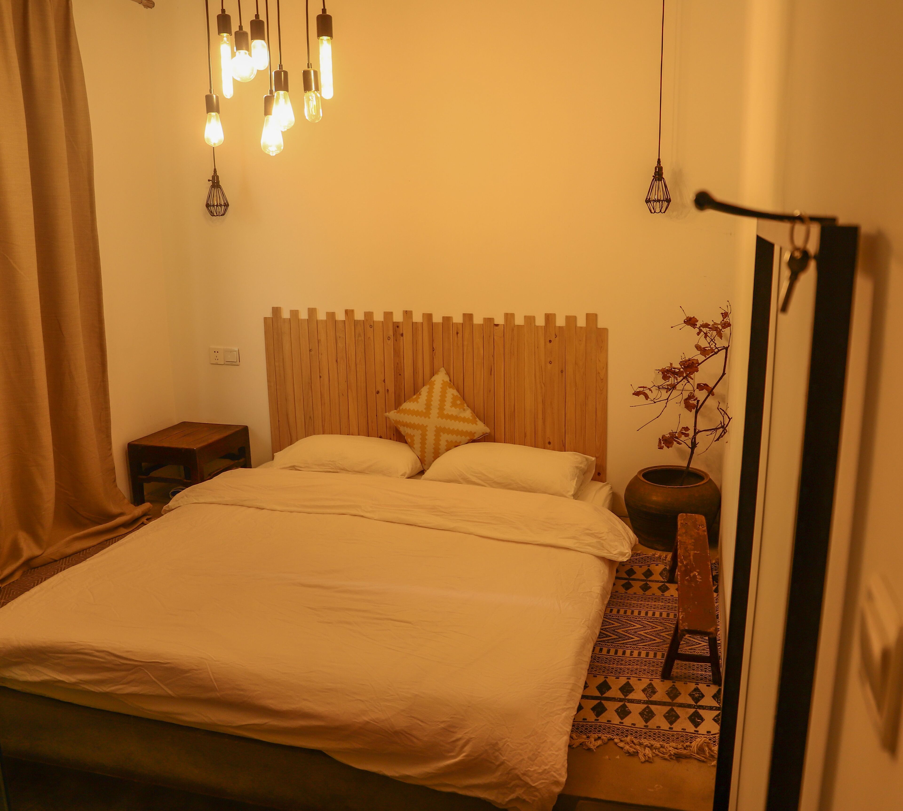 A bedroom with a wooden headboard, a bed with white linens, a bedside table, a lamp, and a decorative vase.