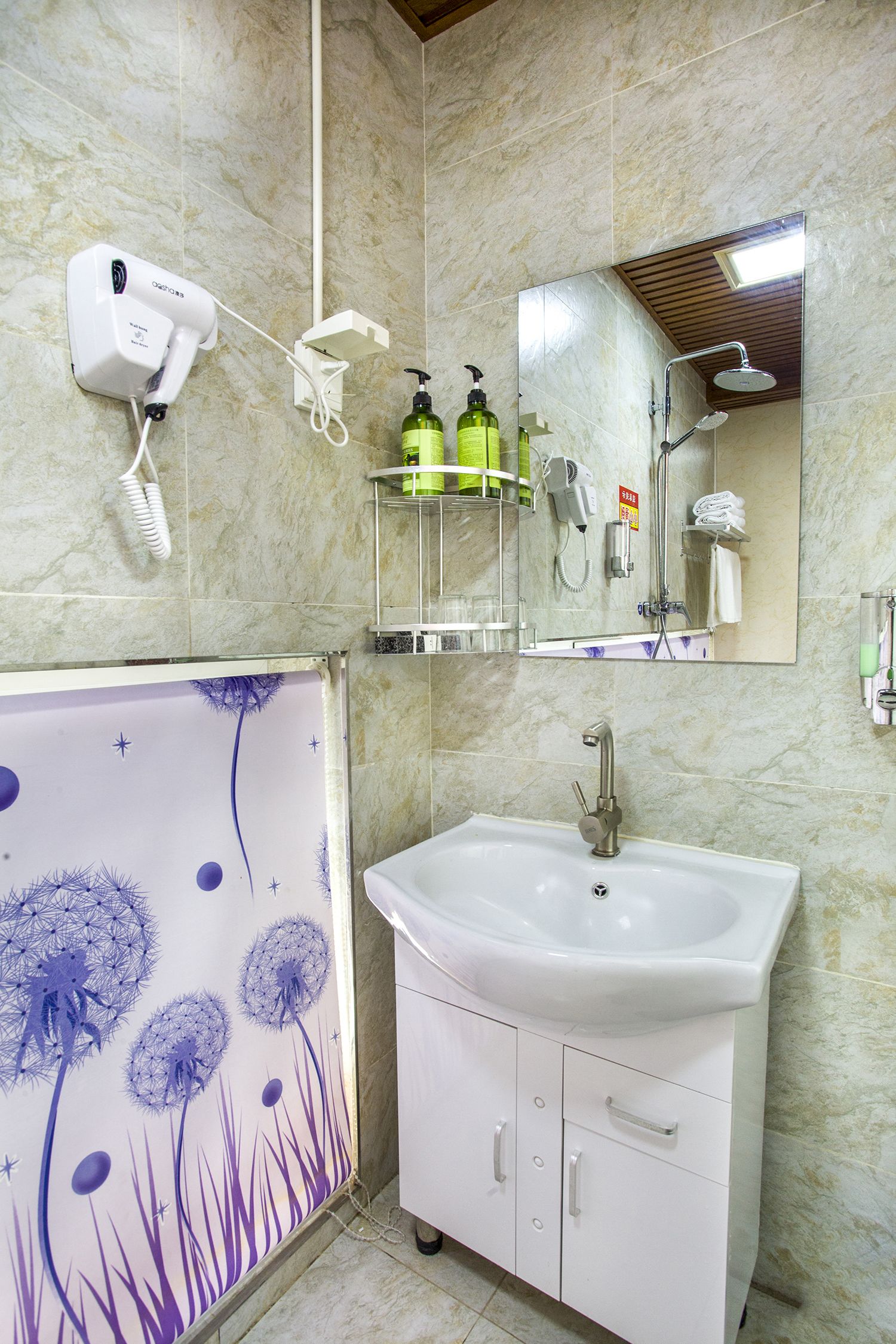 A bathroom with a white sink, a mirror, a shower, and a hairdryer on the wall.