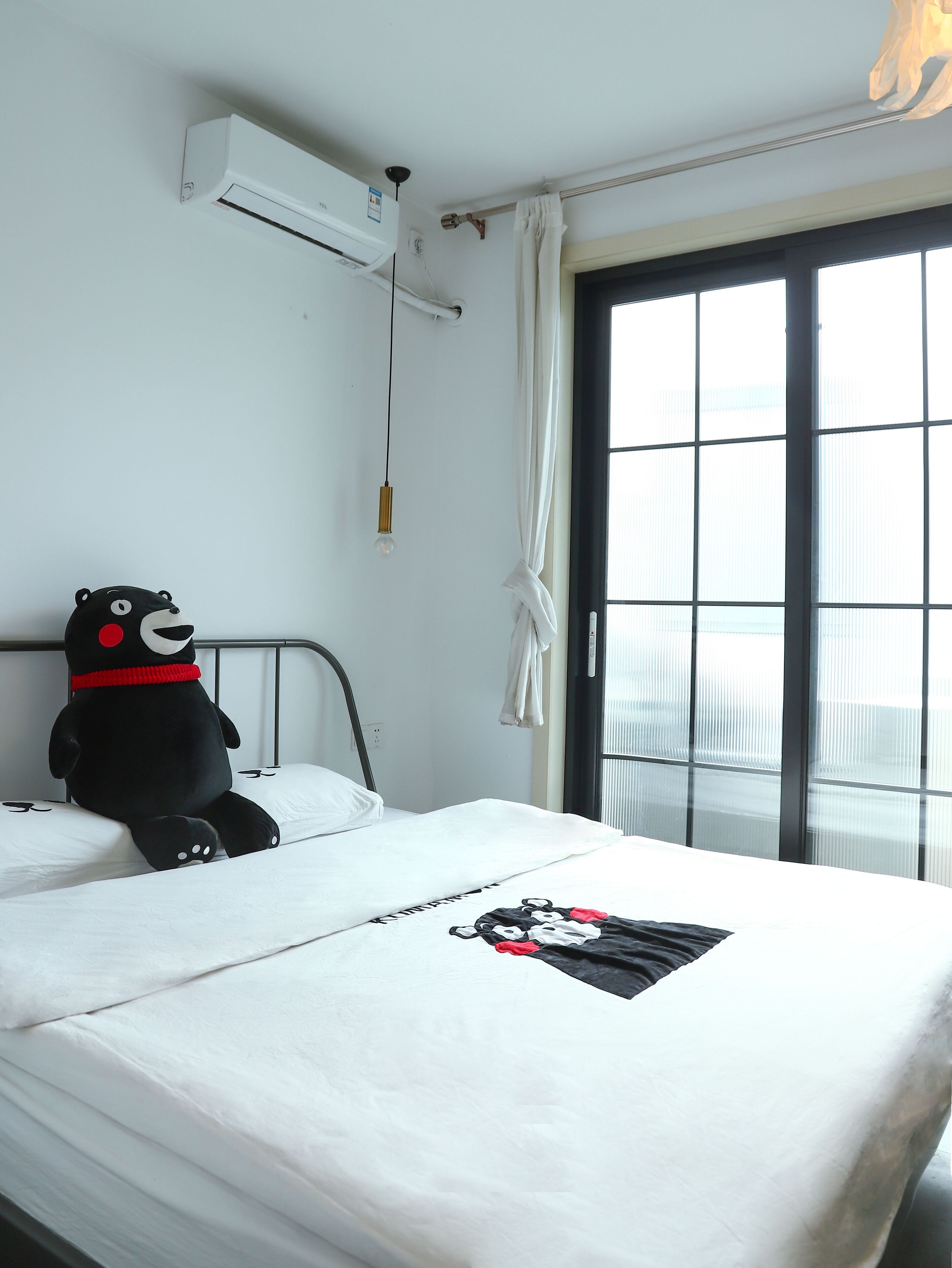 A bed with a white mattress and a black stuffed animal on it. There is a window with curtains and a view of the sky.