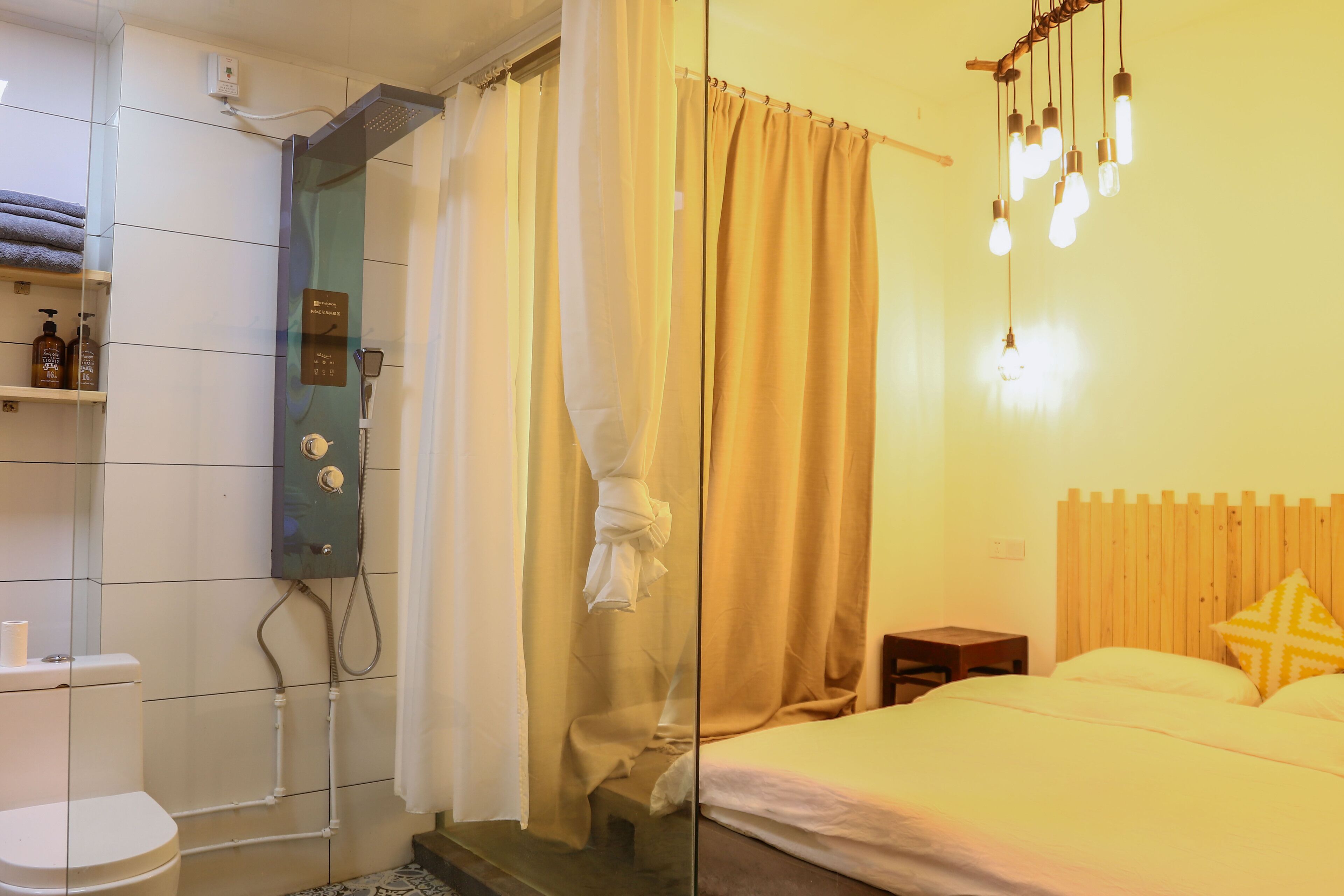 Quarto de hotel com chuveiro, cama, mesa de cabeceira e cabeceira de madeira.