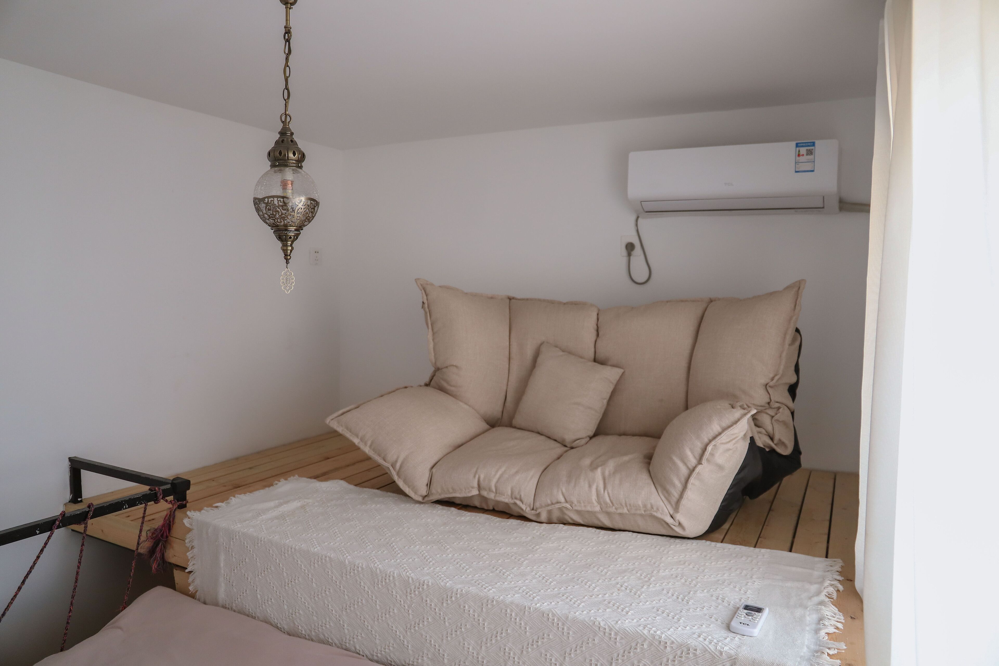 A room with a beige sofa, a white throw blanket, a hanging lamp, and an air conditioning unit.