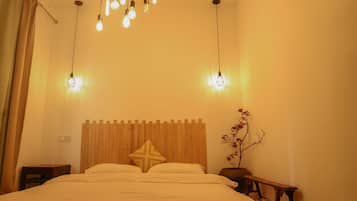 Un dormitorio con cabecera de madera, cama con ropa de cama blanca, mesita de noche, un banco y lámparas colgantes.