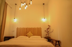 Un dormitorio con cabecera de madera, cama con ropa de cama blanca, mesita de noche, un banco y lámparas colgantes.
