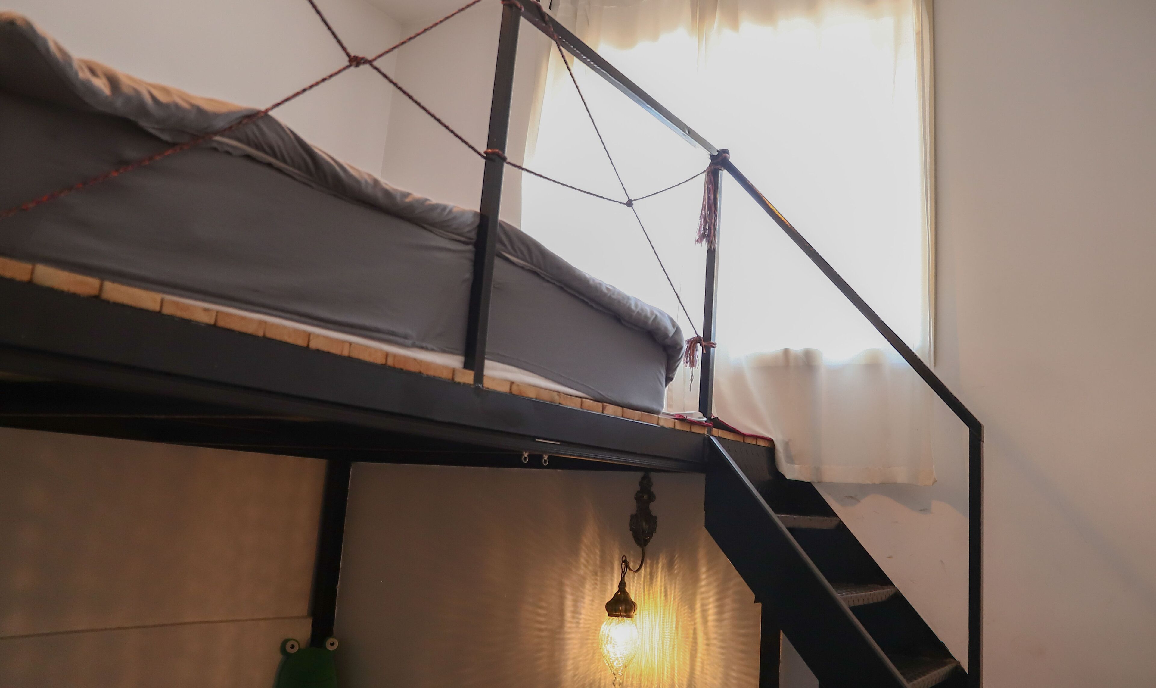 A bunk bed with a ladder, a hanging light fixture, and a window with curtains.