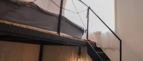 A bunk bed with a ladder, a hanging light fixture, and a window with curtains.