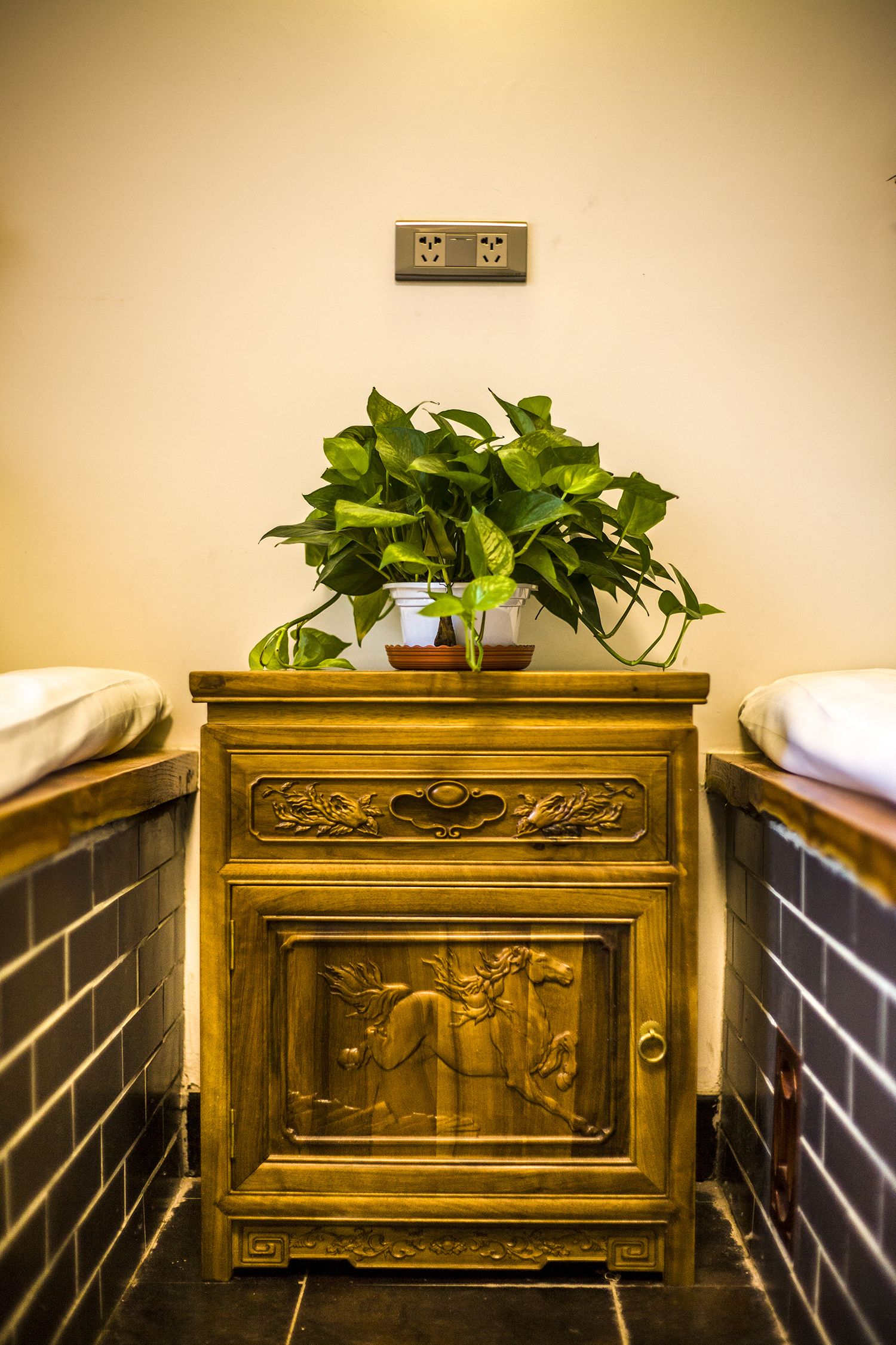 A bathroom with a wooden vanity, a potted plant, and a tiled floor.